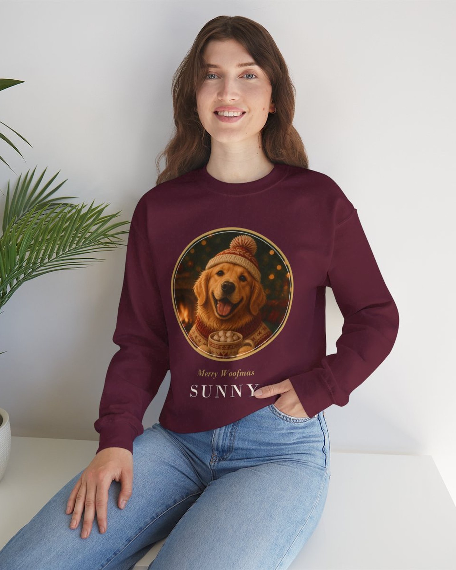 A woman sitting by a plant in the maroon Christmas medallion sweatshirt